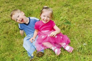 laughing small boy and girl sitting on green grass in the park